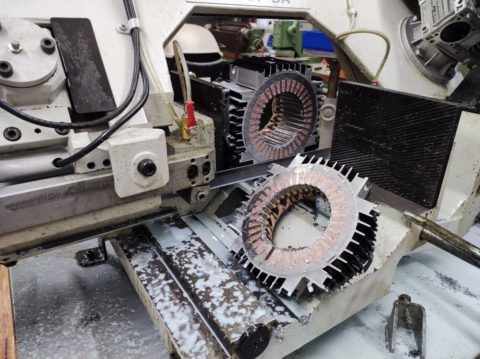 Photograph of two IPMSM stator sections clamped and cut on a metal bandsaw, coolant pooled on the machine bed. Each section shows the 36-slot stator lamination stack with copper conductors packed into the slots, wrapped in a finned aluminium housing.