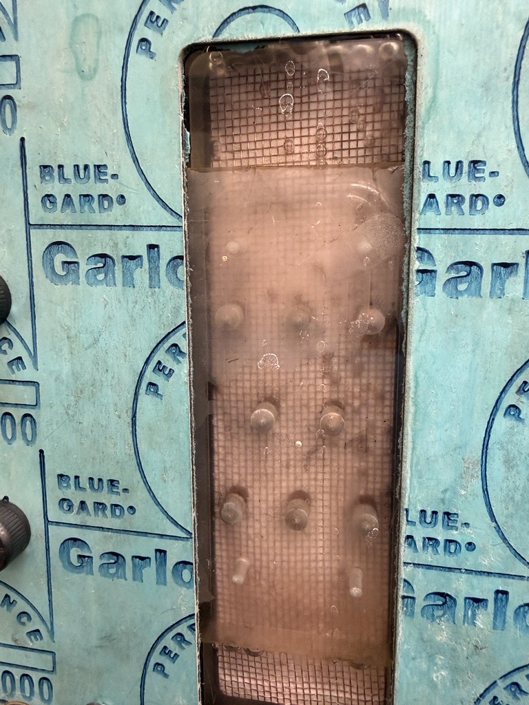 Close-up photograph of the assembled conductive-gap membrane distillation module: copper mesh visible through the machined acrylic channel, sealed with a Garlock Blue-Gard gasket and bolted together.