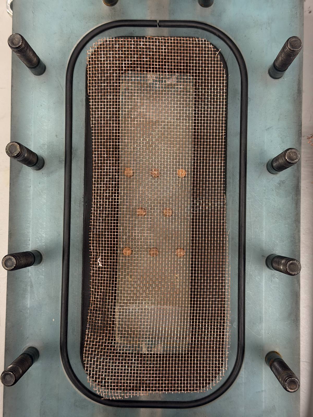 Close-up of the machined feed-side channel with the conductive pin fins installed, copper contacts soldered to the mesh.